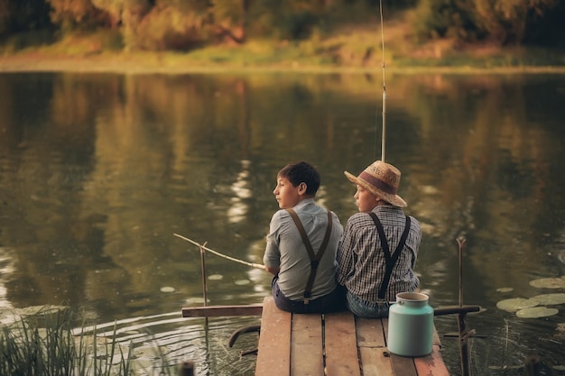 Two boys are fishing on the lake in the village at sunset in summer