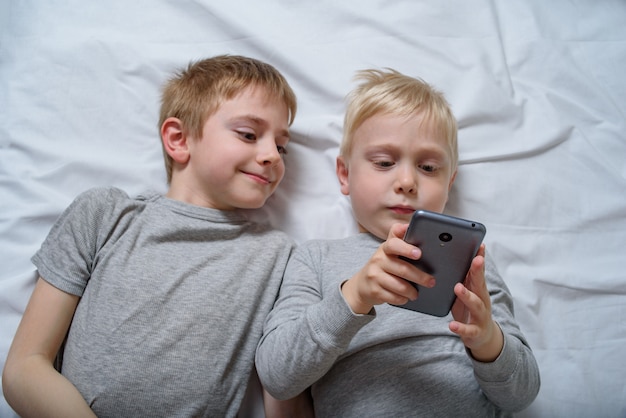 Two boys are lying in bed with a smartphone. Gadget Leisure