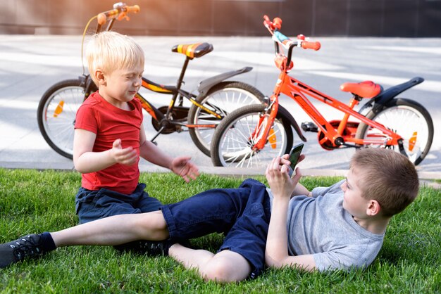 Two boys are photographed on a smartphone while sitting on the grass. Rest after cycling, bicycles