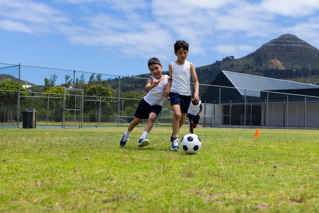 Двое мальчиков играют в футбол в солнечный день в школе, а один гонится за мячом.