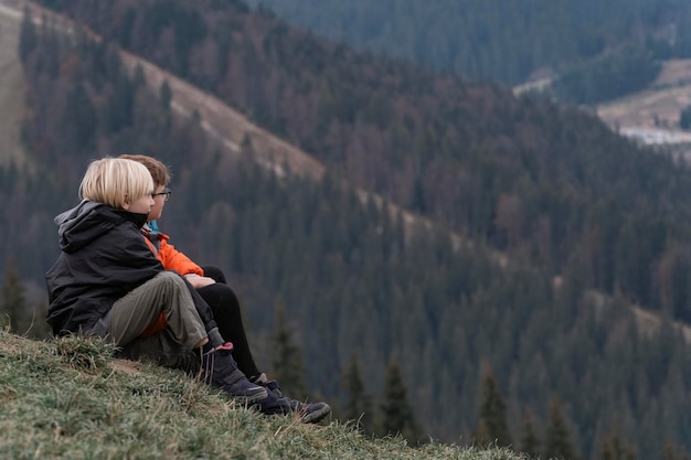 Two boys are sitting on hillside Portrait of children in autumn in the mountains Weekend in nature outside