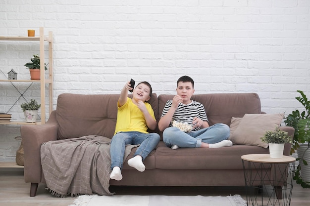 두 소년이 소파에 앉아 팝콘을 먹고 밝은 거실에서 TV를 보고 있습니다.