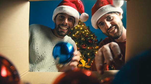 Photo two boys are taking the balls from the box in christmas time against the tree