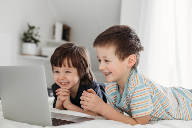 Фото Два мальчика-брата лежат на кровати и смотрят в цифровой ноутбук дистанционного обучения для детей