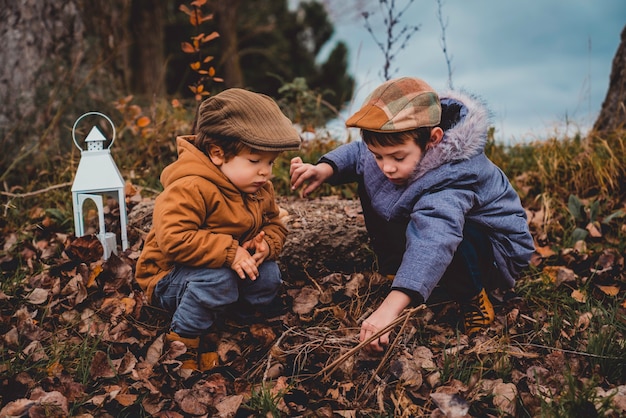 Two boys dressed in coats looking at the fallen leaves in the field on a cloudy day