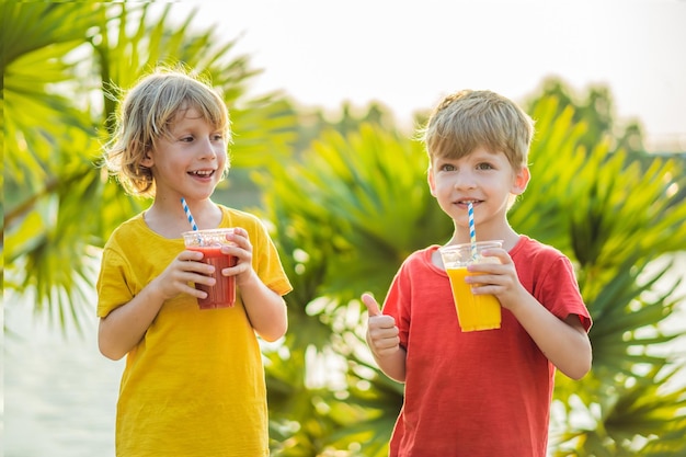 Due ragazzi bevono frullati sani sullo sfondo delle palme frullati di mango e anguria alimentazione sana e vitamine per i bambini