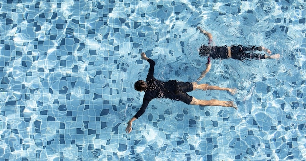 Два мальчика смешно плавают вместе в бассейне с чистой водой, снято с высоты птичьего полета.