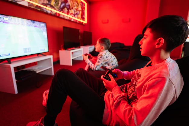 Two boys gamers play football gamepad video game console in red gaming room