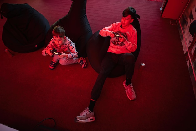 Two boys gamers play gamepad video game console in red gaming room