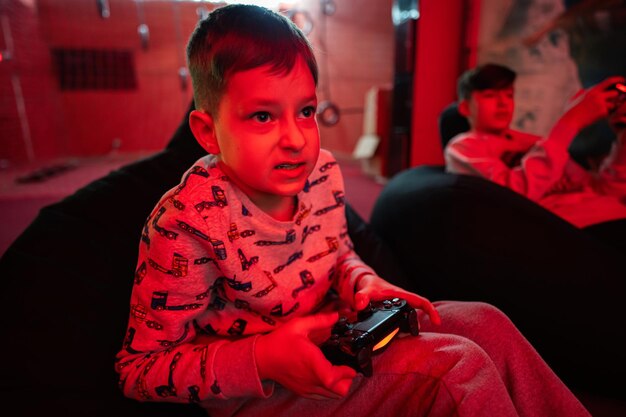 Two boys gamers play gamepad video game console in red gaming room