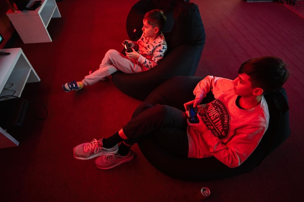 Two boys gamers play gamepad video game console in red gaming room