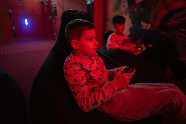 Two boys gamers play gamepad video game console in red gaming room