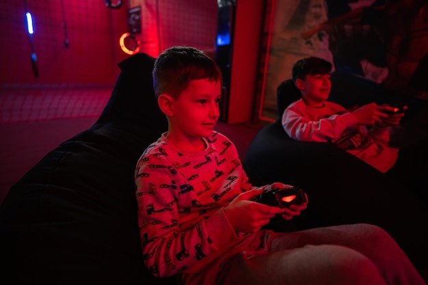 Two boys gamers play gamepad video game console in red gaming room