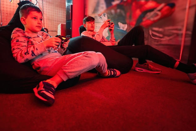 Two boys gamers play gamepad video game console in red gaming room