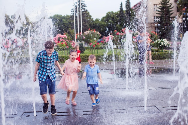 Two boys and a girl are running through streams of water in a fountain warm sunny day