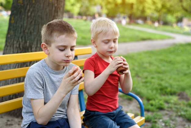 Two boys have a snack on a bench in the park