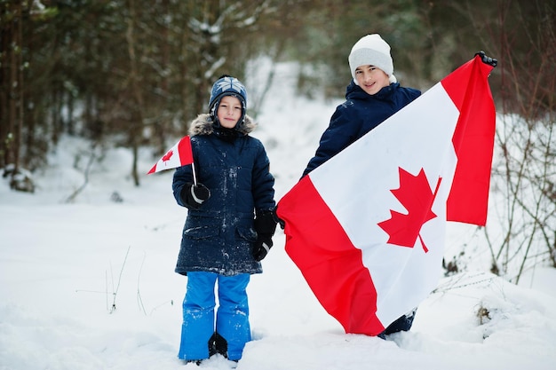 Two boys holding flag of Canada on winter landscape.