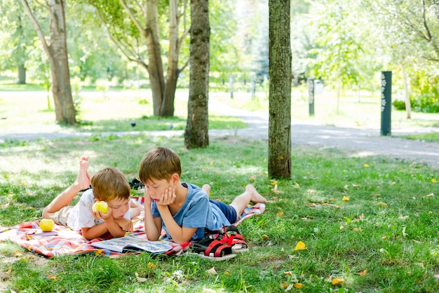 Due ragazzi giacciono su una coperta in un parco verde. i bambini leggono un libro steso a terra, nel parco. bambini in un picnic in estate, leggendo libri. vacanze estive. didattica a distanza in natura.