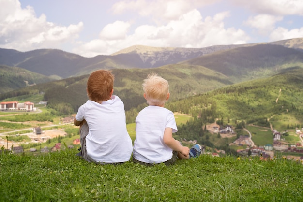 丘の上に座って、山を見て二人の少年。背面図