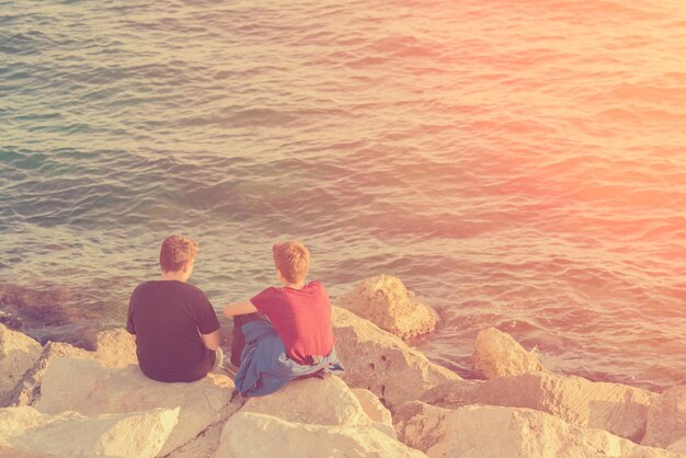 Two boys sitting on the rocks near the water