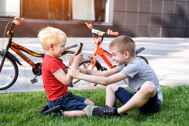 Two boys using a smartphone while sitting on the grass