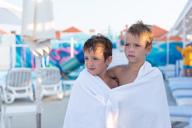 Two boys wrapped in a bath towel after swimming in the outdoor pool