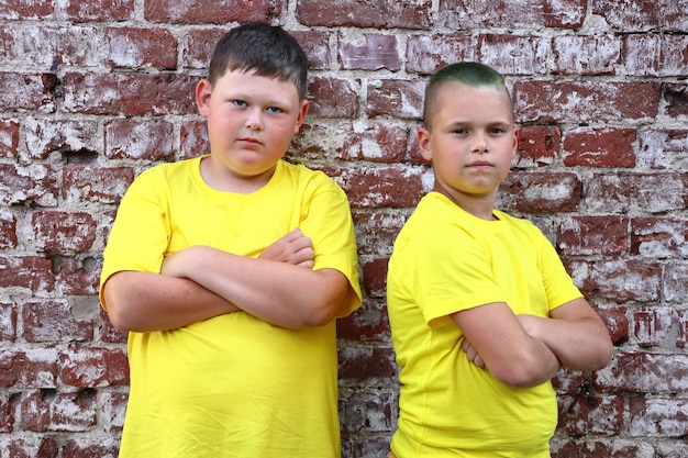 Two boys in yellow T-shirts stand cross-arm at a brick wall. High quality photo