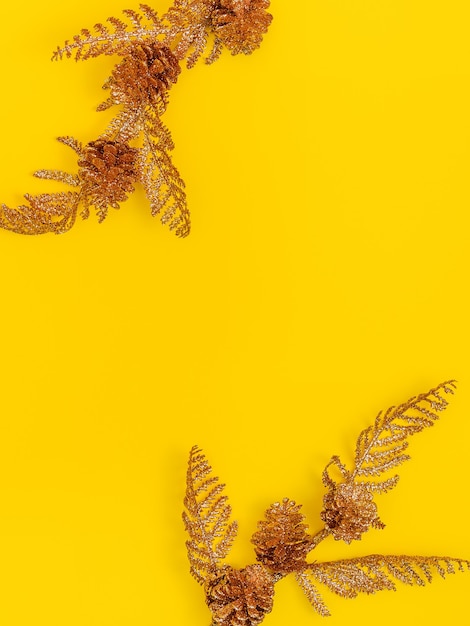 Two branches of a Christmas tree with cones, covered with golden shiny paint, on a yellow background. Copy space in the center, flat lay