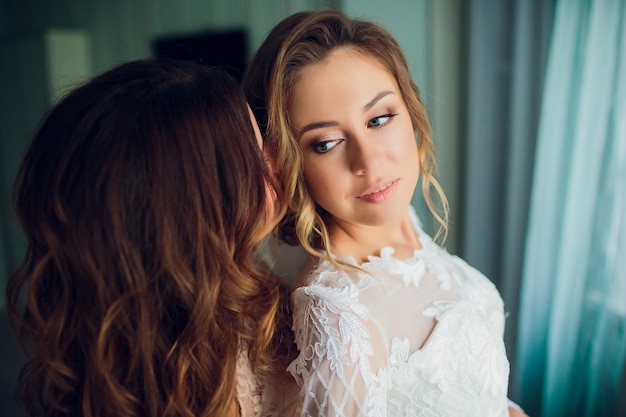 Two brides are whispering about something and laughing. Beautiful delicate Girls in wedding dresses.