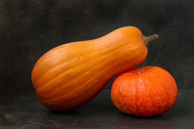 Photo two bright mature pumpkins are located on a dark background, horizontal orientation, closeup