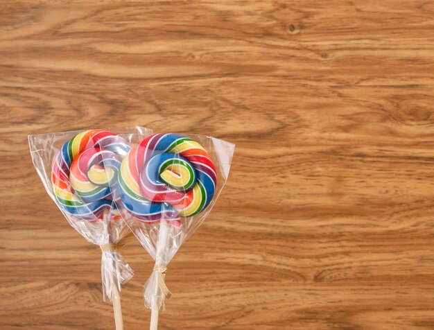 Photo two brightly colored lollipops in a transparent package on a wooden background copy space for text