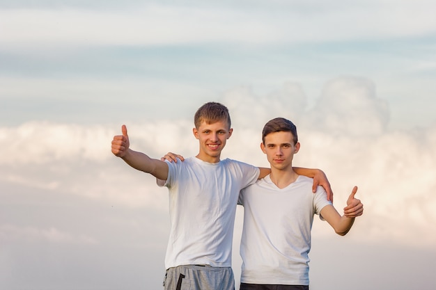 Two brother guys stand against the sky happy.