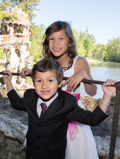 Two brother and sister children at the edge of a lake are dressed for the birthday or ceremony