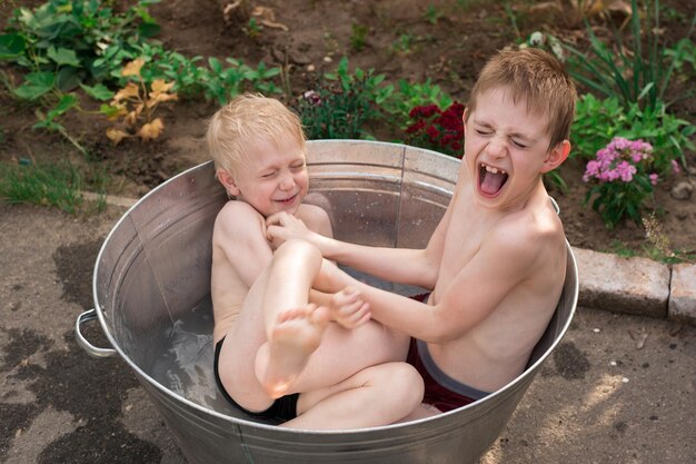 Two brothers bathe in basin outdoors Siblings play splash