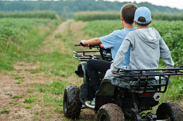 Two brothers driving four-wheller ATV quad bike. Happy children moments.