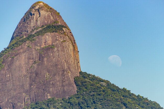 Photo two brothers hill with the moon setting in rio de janeiro.