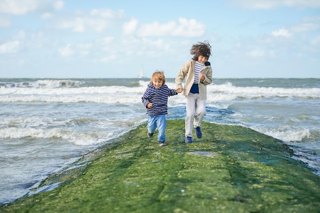 Photo two brothers holding hands are running on a breakwater at the north sea laughing boys spending weekend at the seaside in belgium knokke siblings friendship