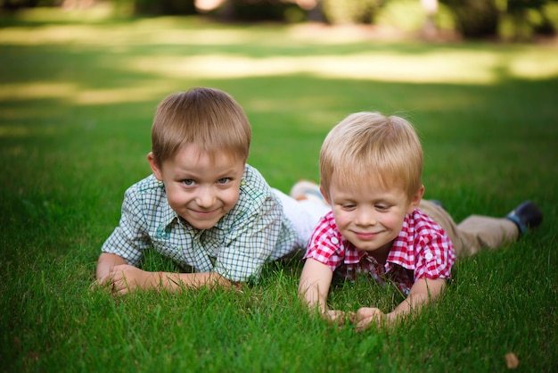 Two brothers lying on the grass in a park outdoors, smiling and