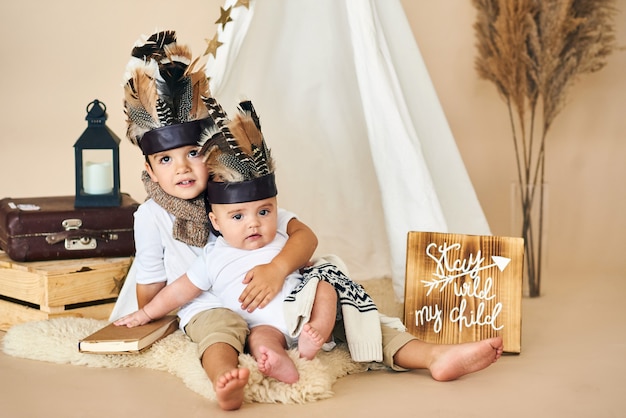 Two brothers playing indian in tent on beige background