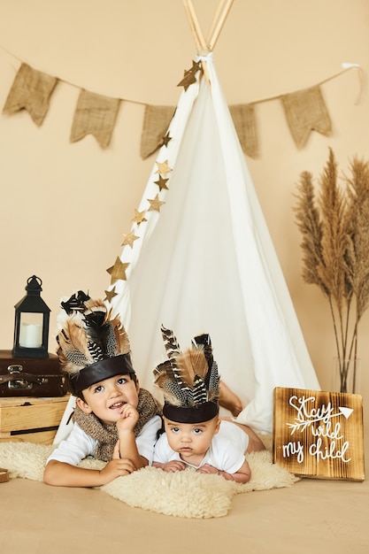 Two brothers playing indian in tent on beige background