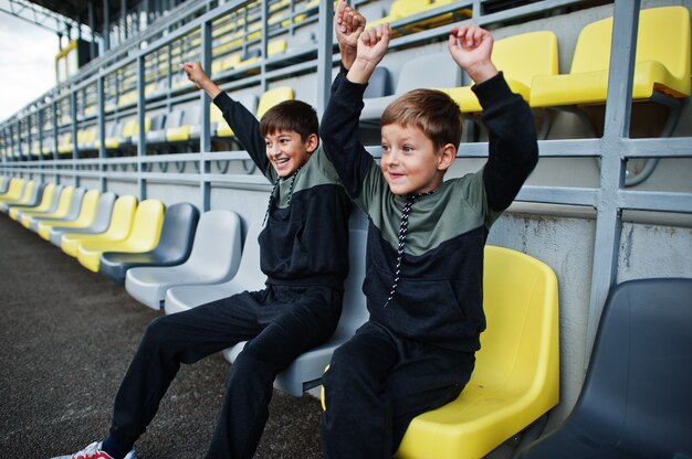 Two brothers support their favorite team, sitting on the sports podium at the stadium.