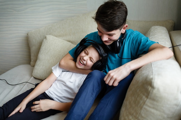 Two brothers together listen to music on headphones at home on the couch