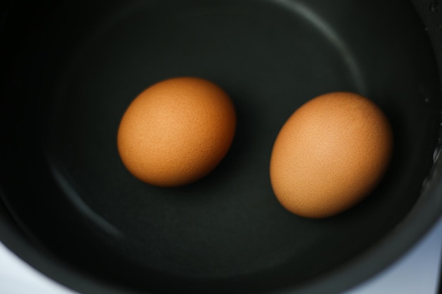 Two brown eggs in a pot of water on the stove