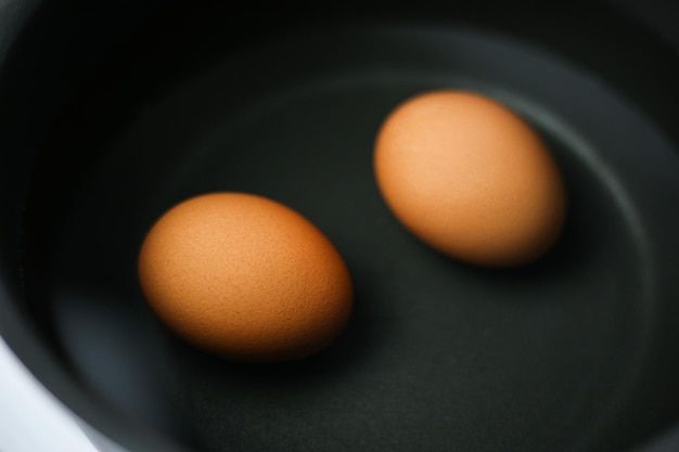 Two brown eggs in a pot of water on the stove