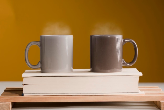 Two brown and gray cups of coffee or tea with hot steam on the table with book and brown background