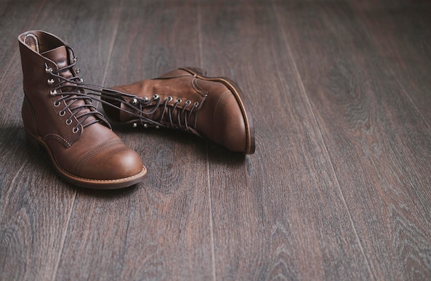 Two brown work leather men laced boots tied to each other on a wooden floor