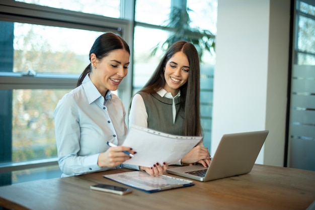 Two brunette business women discussing paper document at office