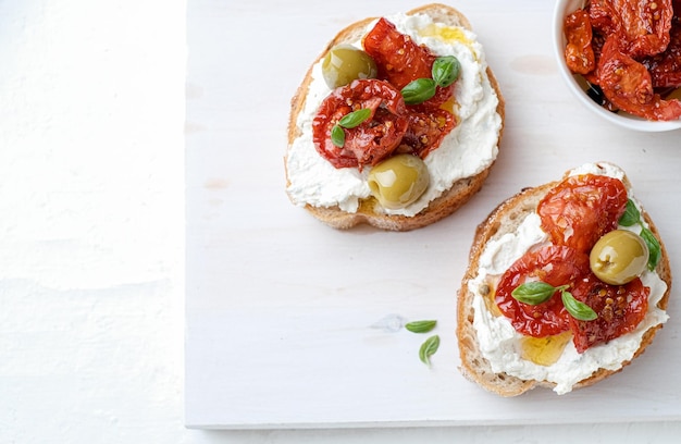 Foto due bruschette con ricotta, olive e pomodori secchi su ciabatta su fondo bianco