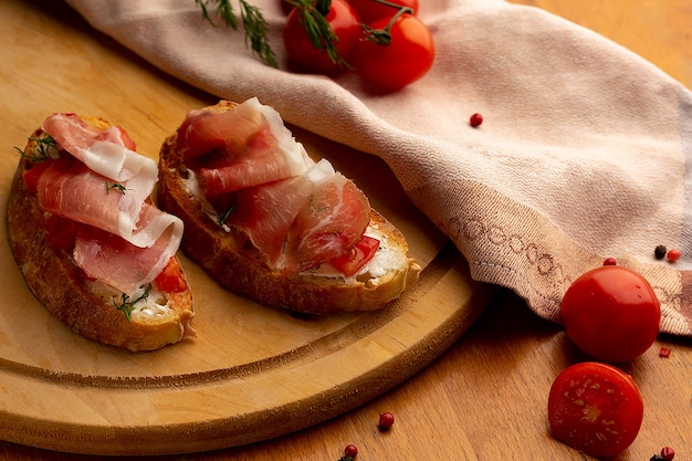 Foto due bruschette con pomodoro e prosciutto su una tavola di legno accanto a un tovagliolo e pomodorini