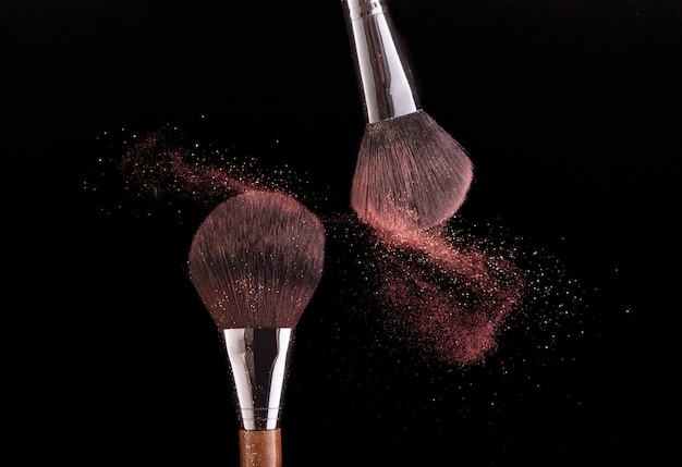 Photo two brushes spraying powder on a black background.